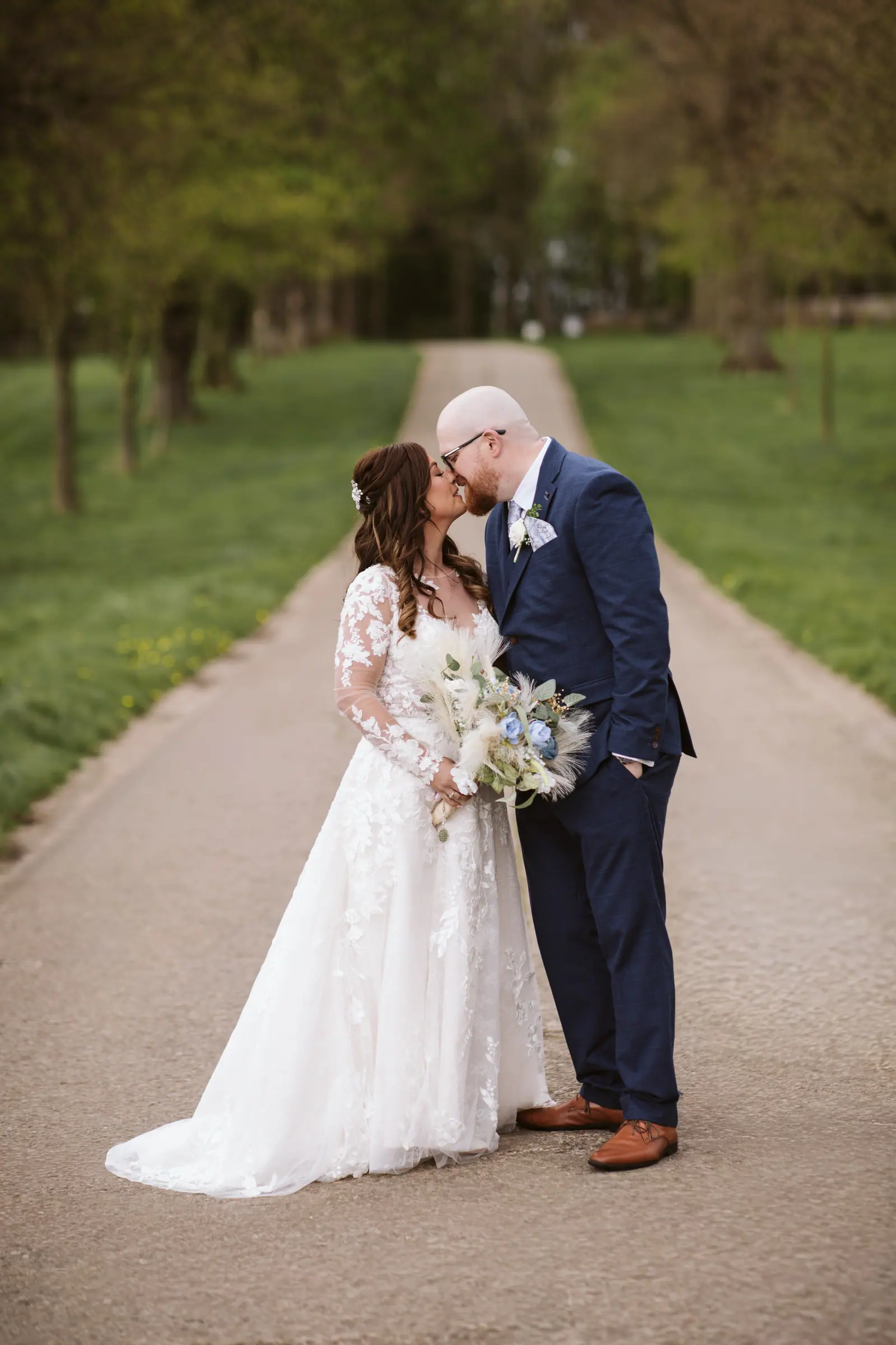Lisa and Dean standing together along the tree-lined venue approach